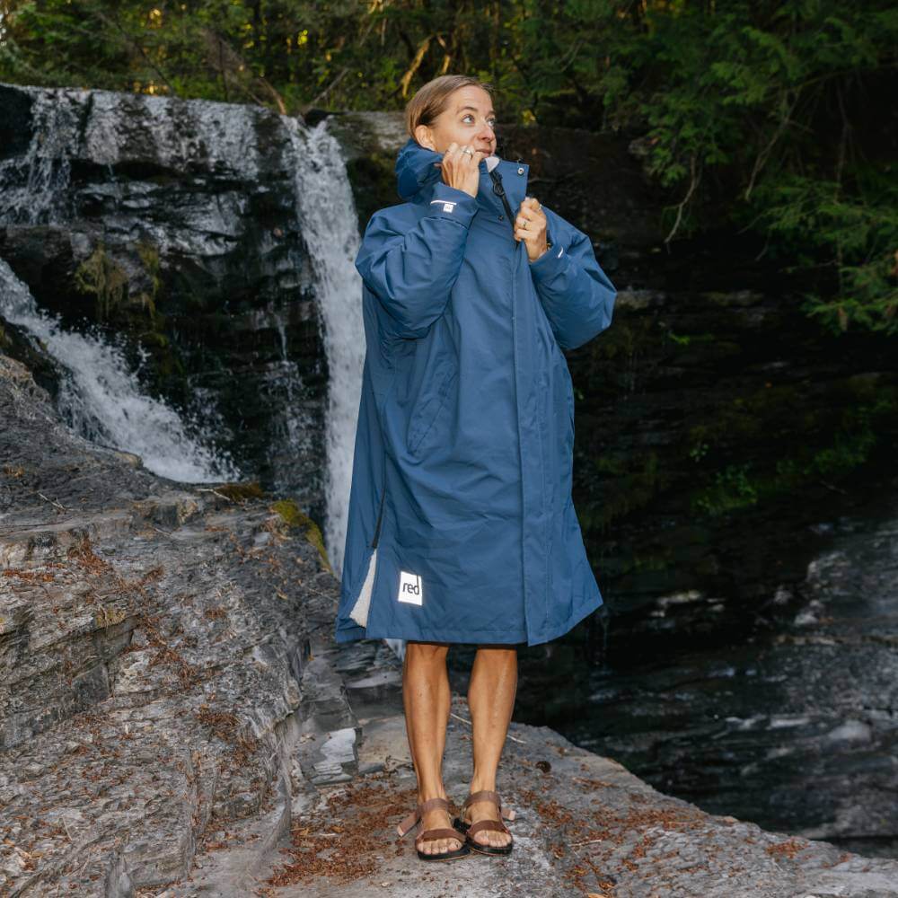 Woman in front of a small waterfall, wearing a Red Alter Evo long sleeve waterproof changing robe in Admiral Blue on an outdoor adventure.