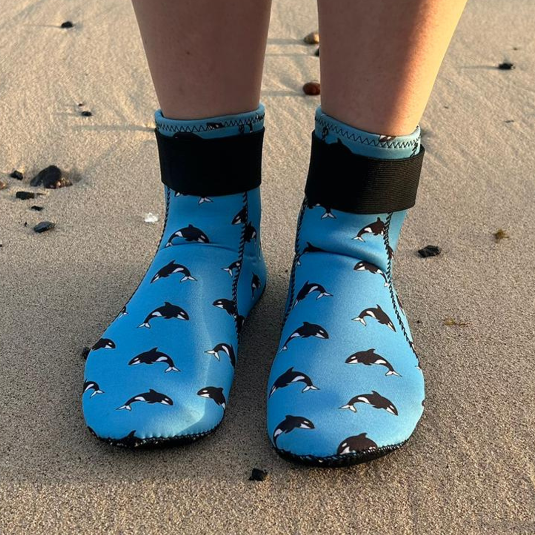 Blue neoprenebeach shoes with  orca pattern worn on sandy ground