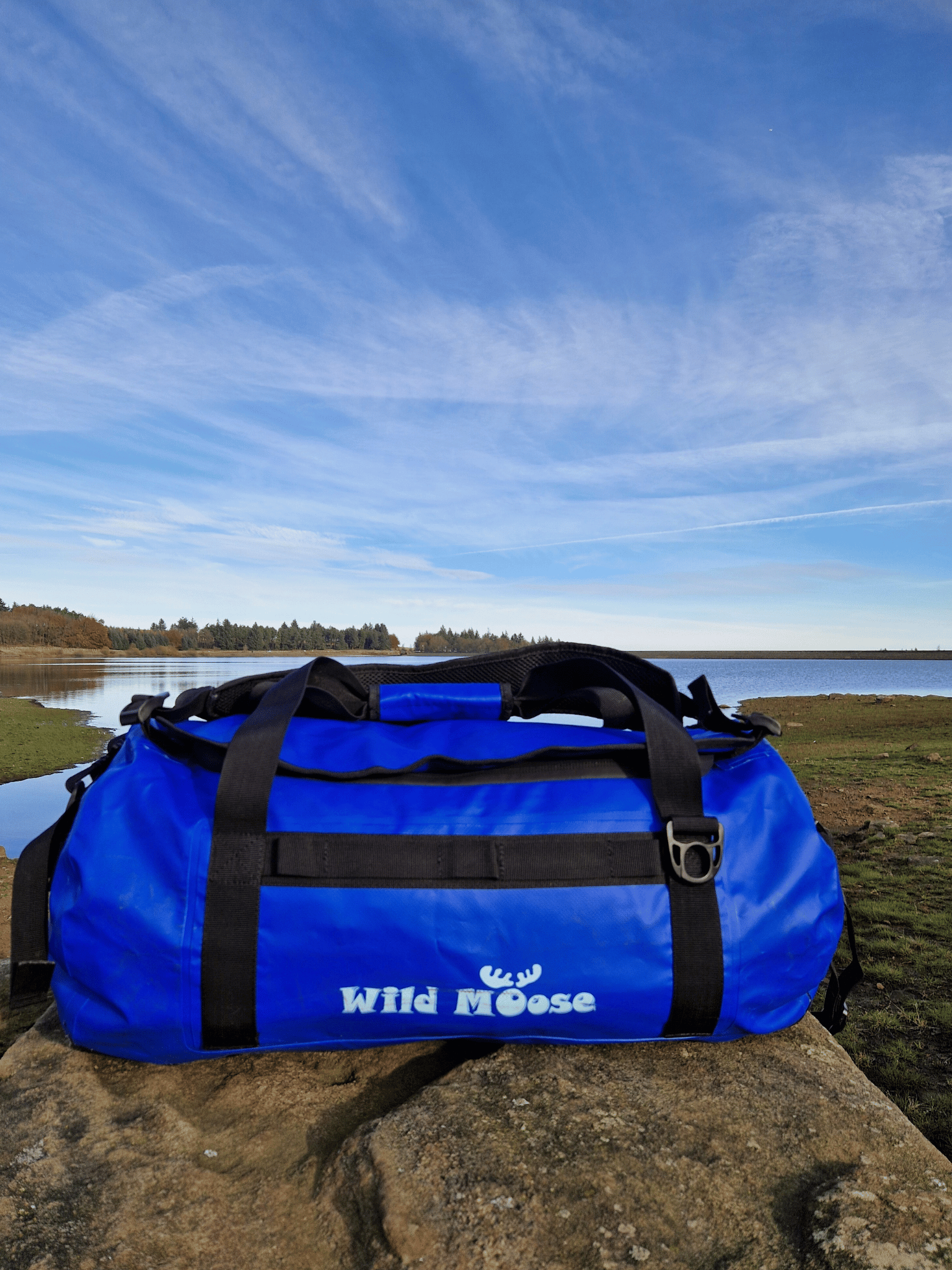 electric blue duffel bag on a rock with water behind