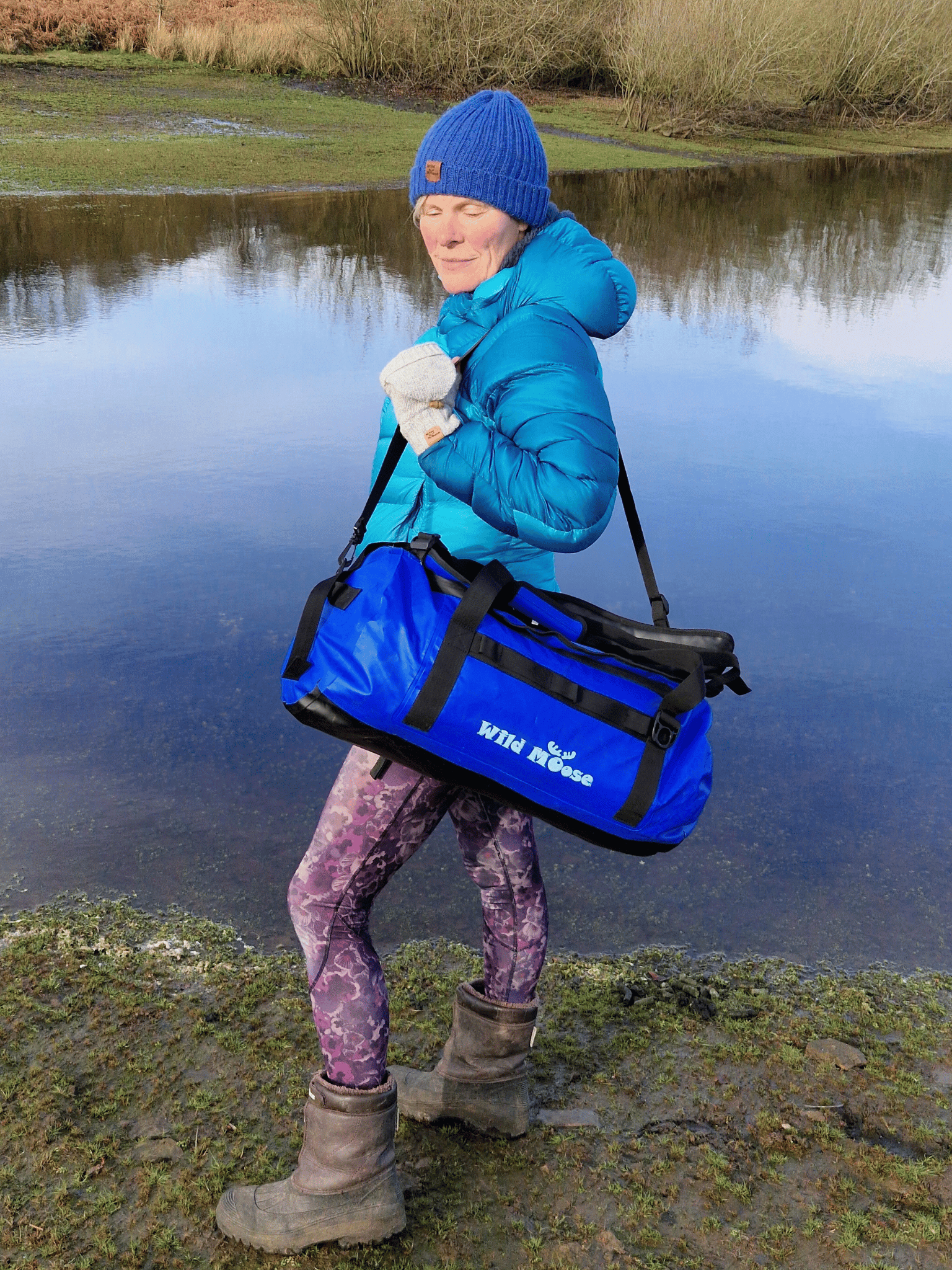 lady stood by water carrying an electric blue duffel bag on her shoulder