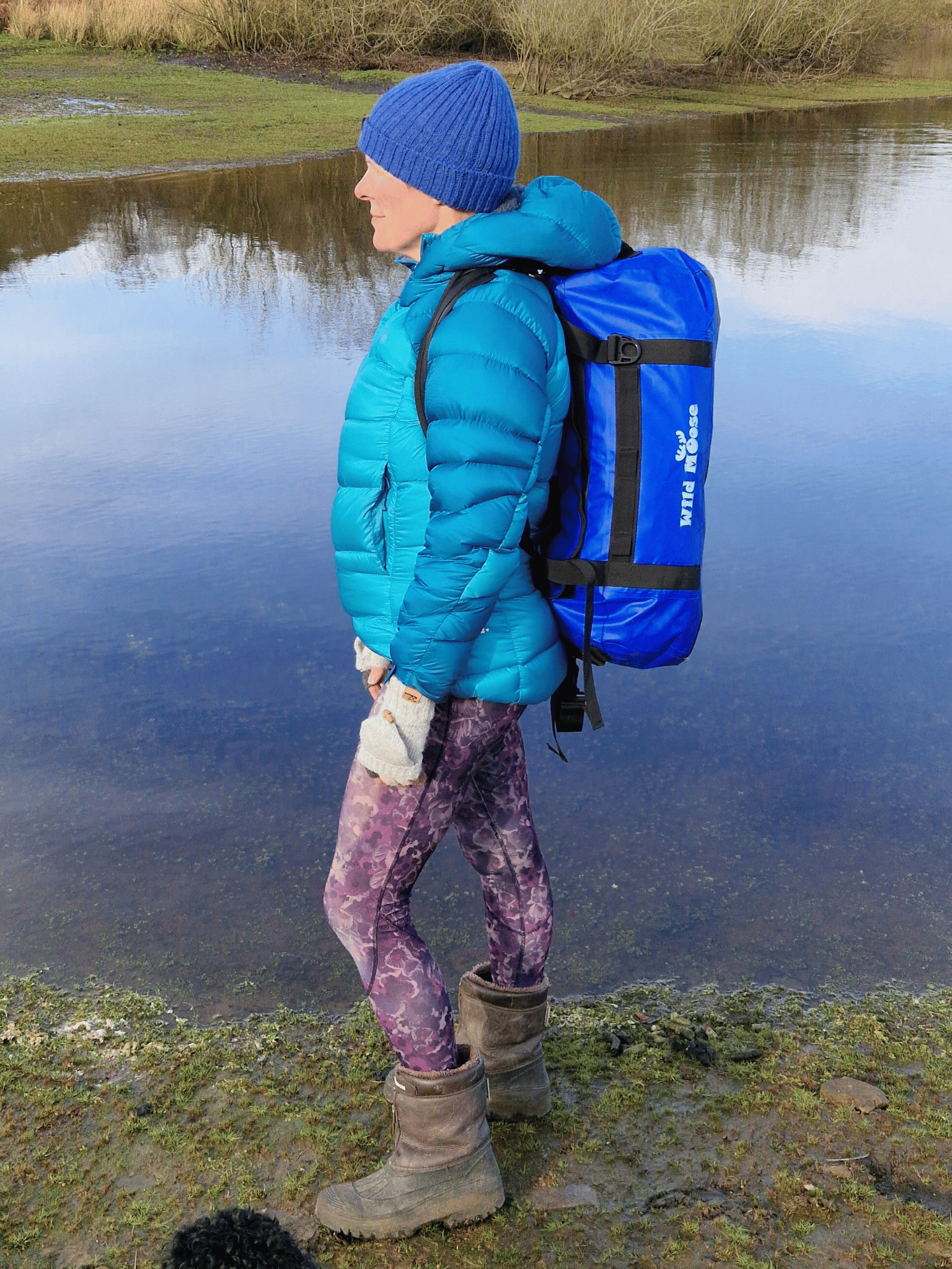 lady stood by water carrying an electric blue duffel bag on her back