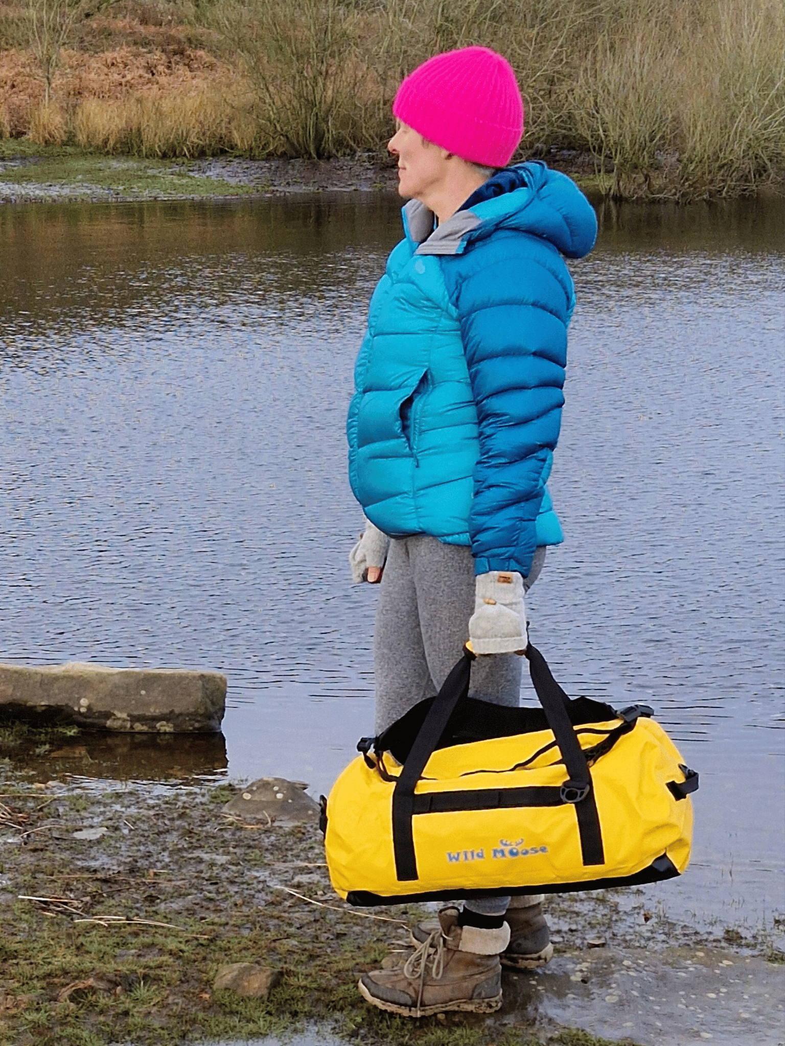 lady stood by water carrying a bright yellow duffel bag in her hand