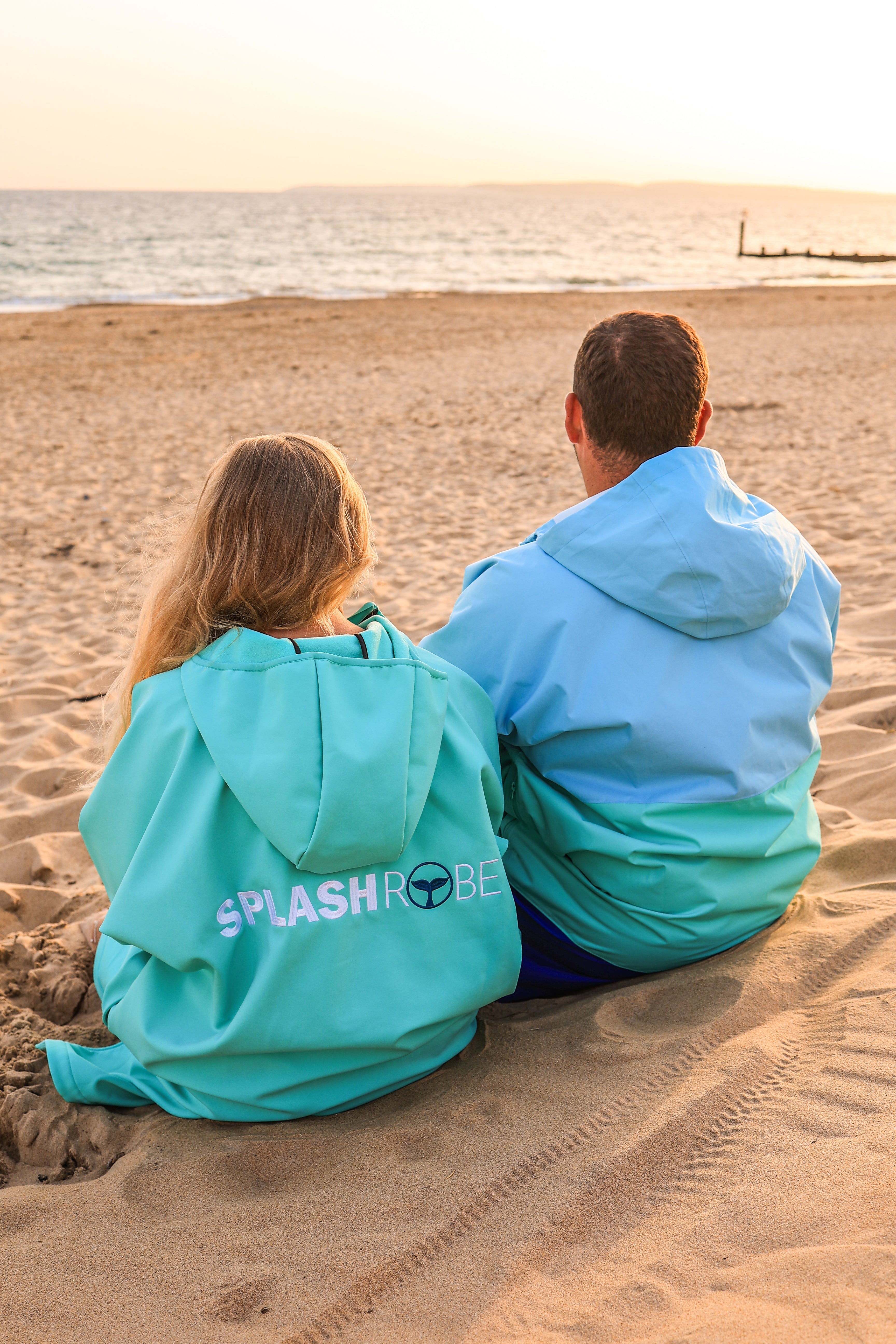 Female wearing inner splashrobe, male wearing outer splashrobe sitting on beach watching the sunset