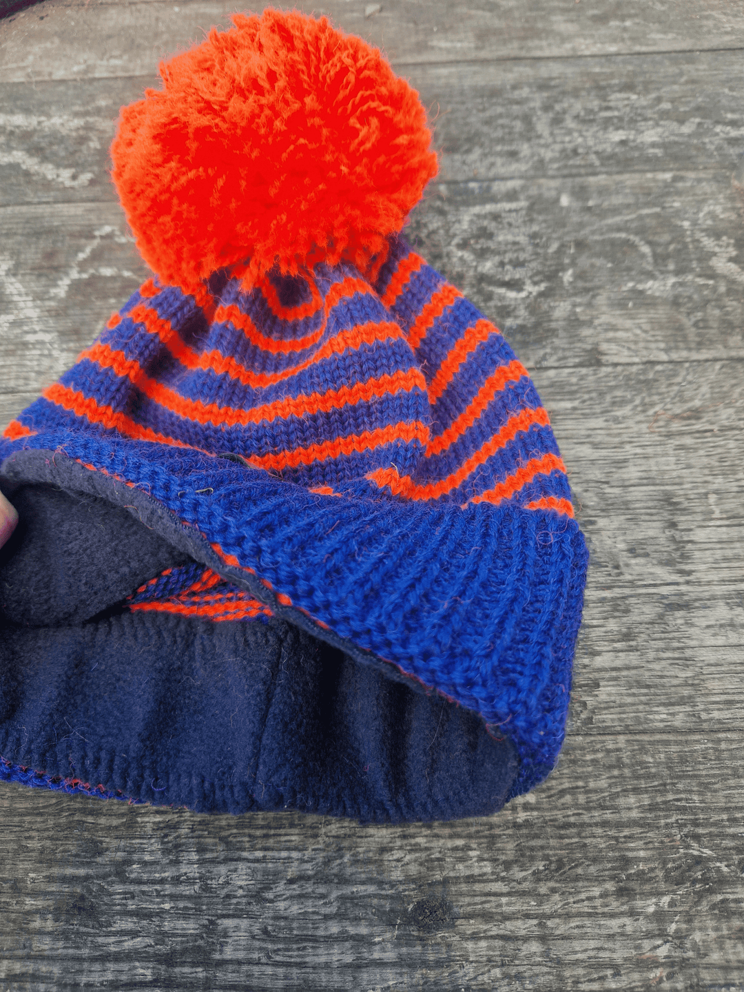 showing the black fleece lining of a blue and orange striped bobble hat
