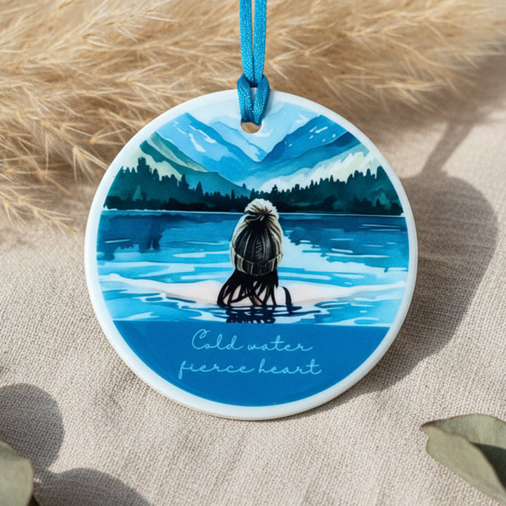 Circular ornament with a painting of a person in a kayak on a lake, surrounded by mountains.
