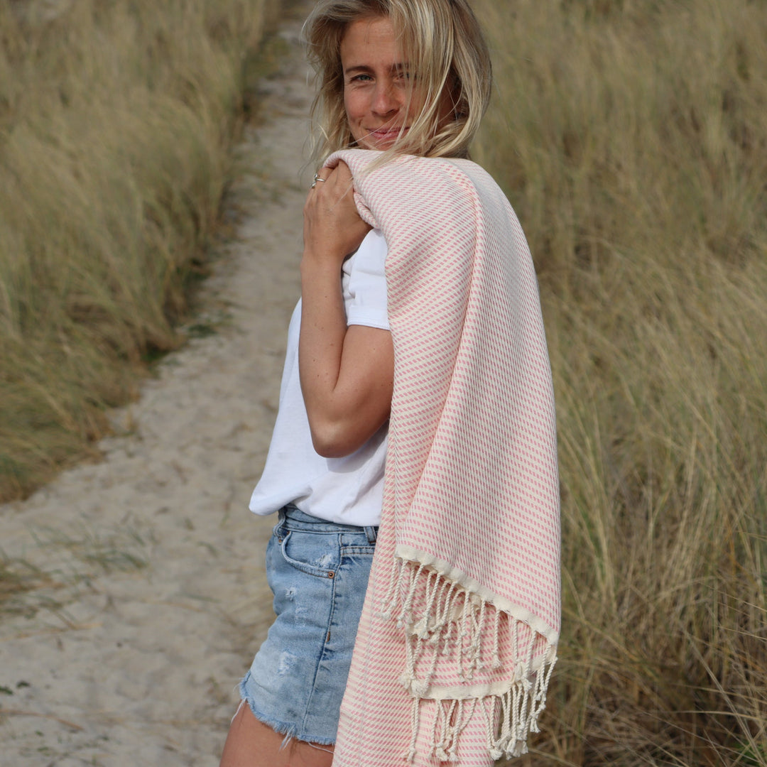 A woman standing in the dunes, with an Ebbflow Cornwall 100% cotton Logan hammam towel thrown over her shoulder