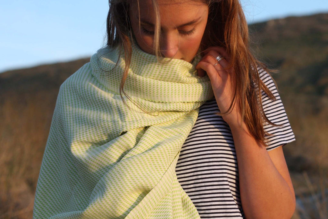 Woman in  stripey t-shirt with a lightweight EbbFlow Cornwall lime hammam towel wrapped around neck and shoulder