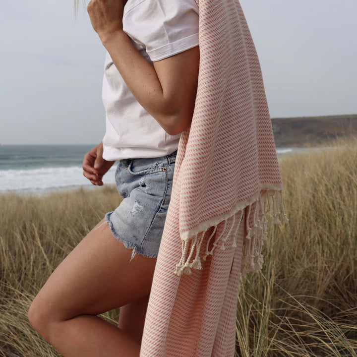 Woman standing in dunes with a pink Logan hammam towel from EbbFlow Cornwall thrown over her left shoulder