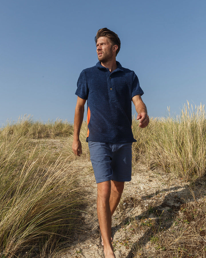 So English Bond polo shirt in navy and orange, featuring a casual fit and classic design, worn in a beachwear setting.
