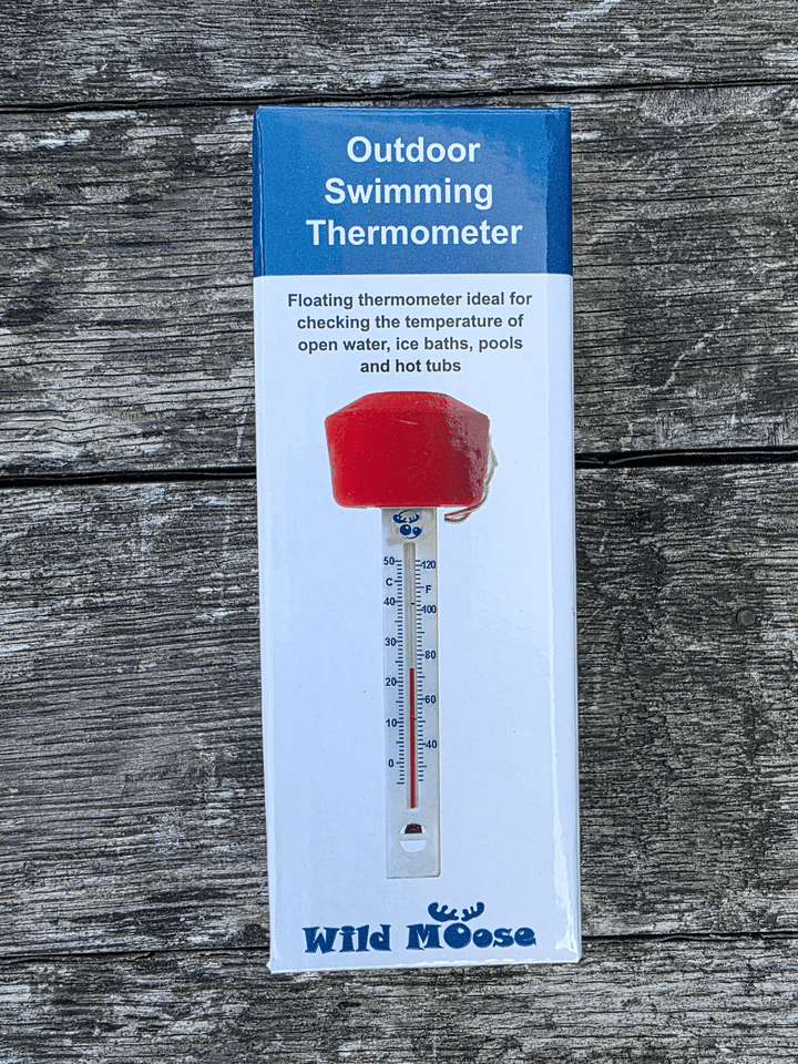 Packaged outdoor swimming thermometer by Wild Moose, featuring an orange float with a white thermometer tube printed on the box, set against a weathered grey wood background.
