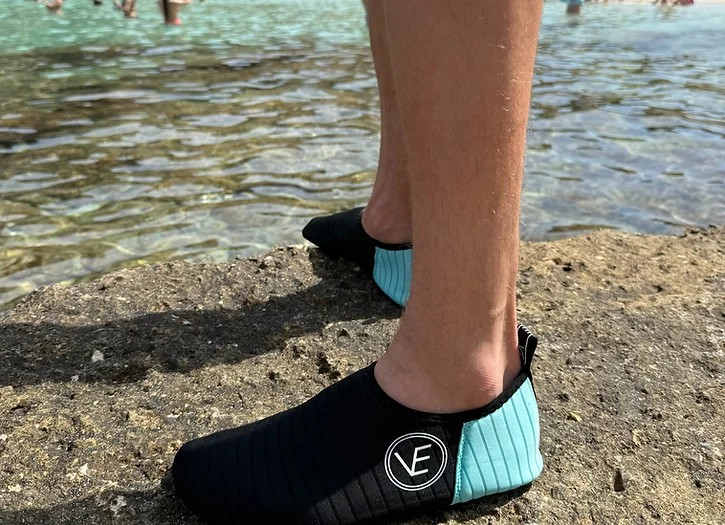 Person wearing a pair of adult water shoes with black and aqua upper and black sole, featuring a distinctive VE logo.