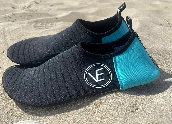 Pair of adult water shoes with black and aqua upper and black sole, featuring a distinctive VE logo on a beach.
