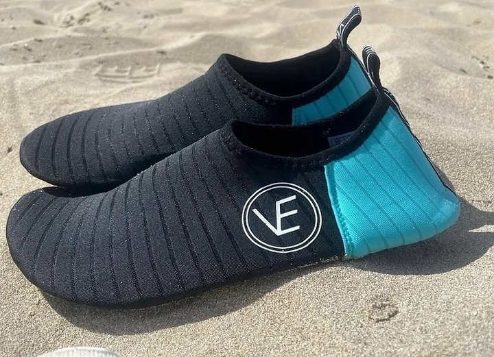 Pair of adult water shoes with black and aqua upper and black sole, featuring a distinctive VE logo on a beach.
