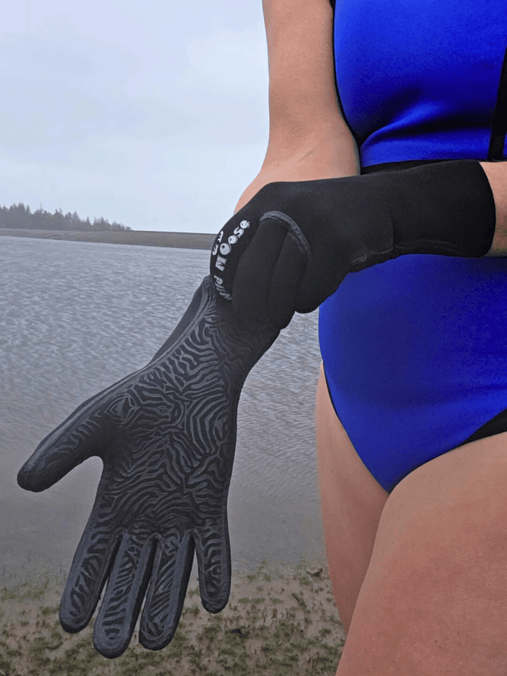 Person wearing a blue wetsuit and black neoprene gloves by a body of water