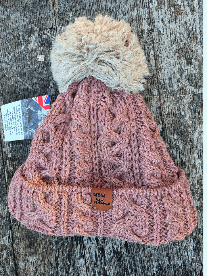 Dusty pink knitted bobble hat with a beige pom-pom on a wooden surface