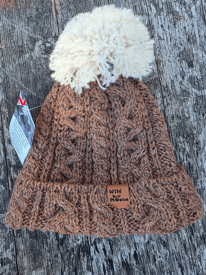 Brown knitted beanie with a white pom-pom on a wooden surface