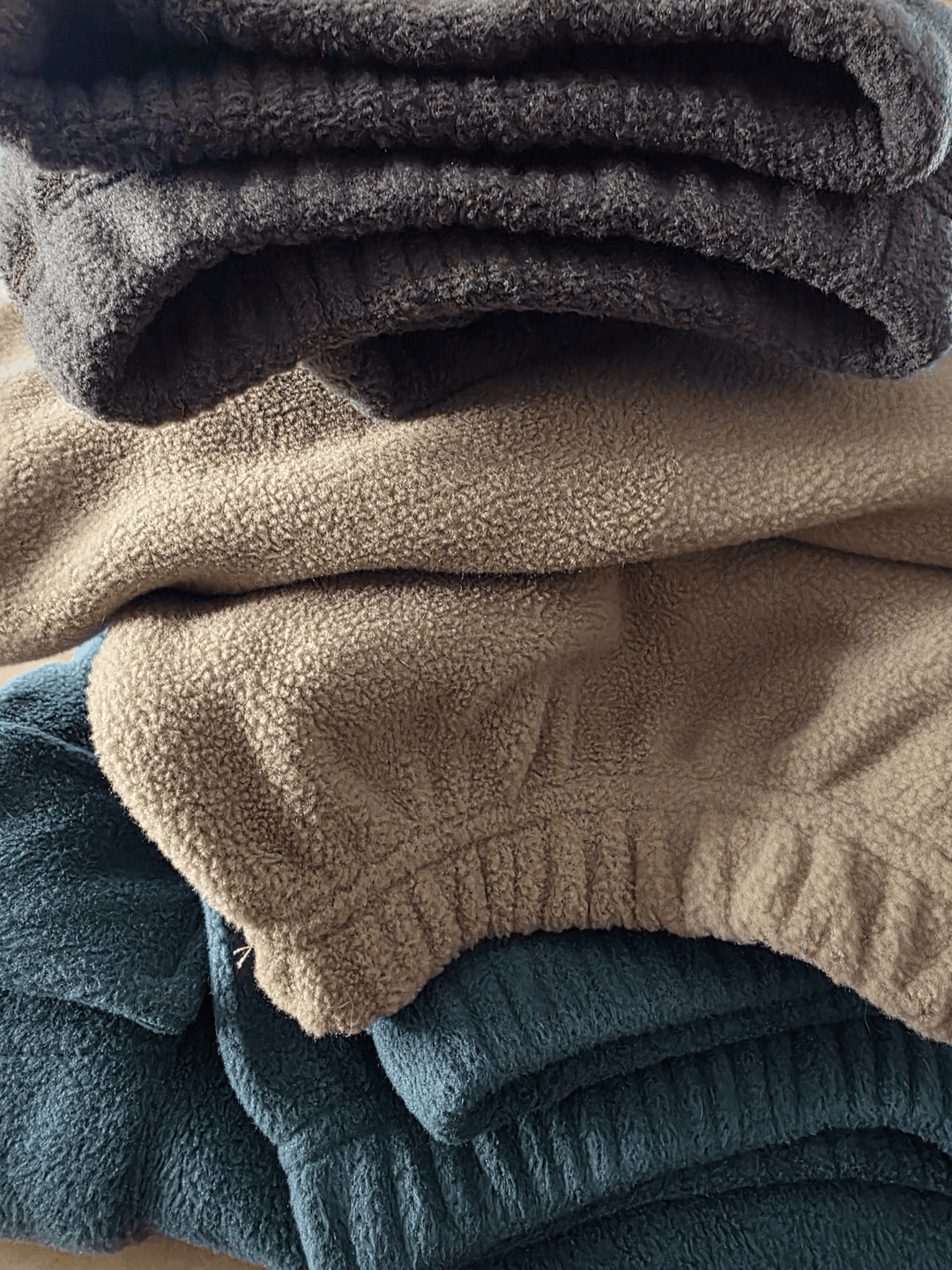 Stack of folded  fleece jogging pants in Petrol Blue, Sand Storm and Charcoal Grey