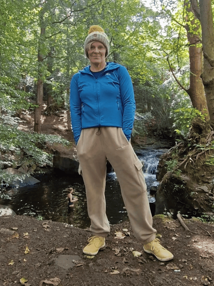 Person standing in a forest wearing beige fleece jogging pants with a stream and waterfall in the background