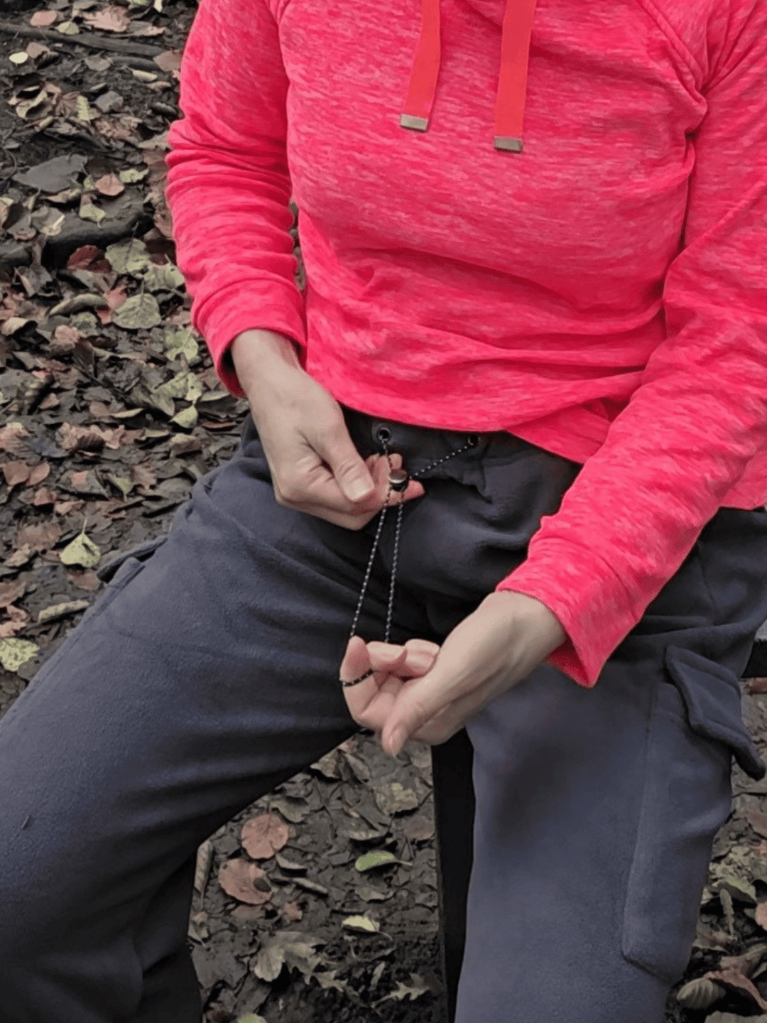 Person wearing dark grey fleece jogging pants sitting on a bench and pulling the drawstring fastening.