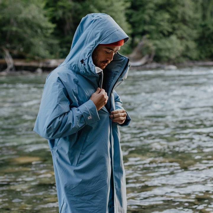 Swimmer wearing a Red Alter Evo men’s long sleeve waterproof changing robe in Alpine Blue by a river after a cold water swim.