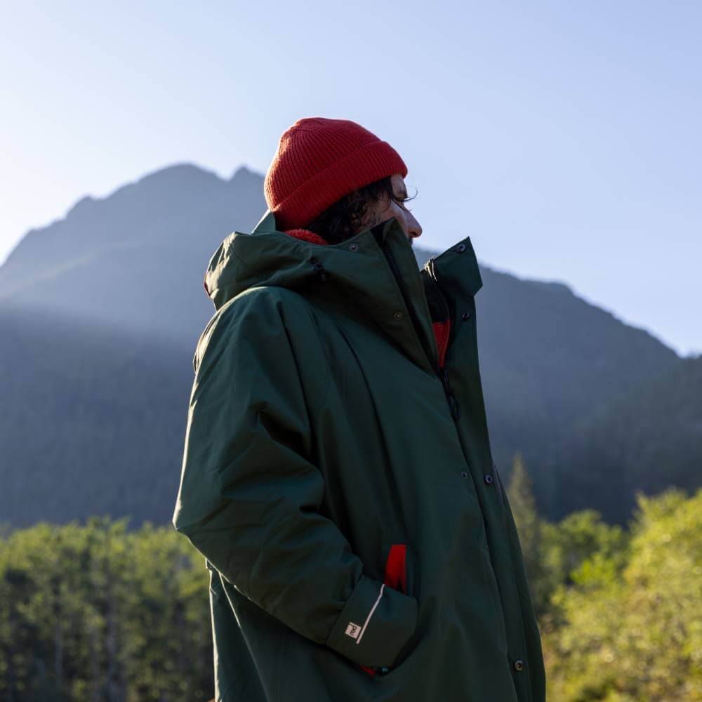 Autumnal lifestyle image of a man wearing a Red Alter Evo long sleeve waterproof changing robe in Forest Green against a backdrop of green mountains.
