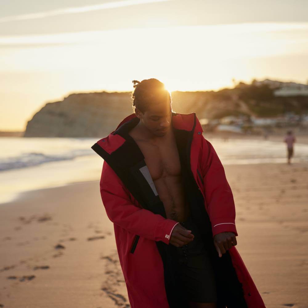Swimmer wearing a Red Alter Evo men’s long sleeve waterproof changing robe in Siren Red on the beach.