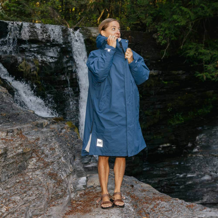 Woman in front of a small waterfall, wearing a Red Alter Evo long sleeve waterproof changing robe in Admiral Blue on an outdoor adventure.