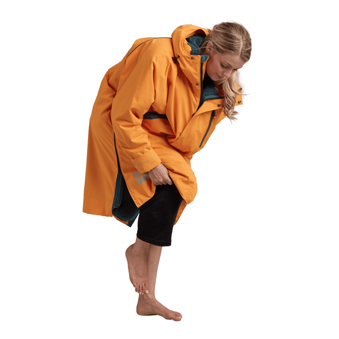 Side profile of a woman changing underneath the Red Alter Evo long sleeve waterproof changing robe in Bitter Orange.