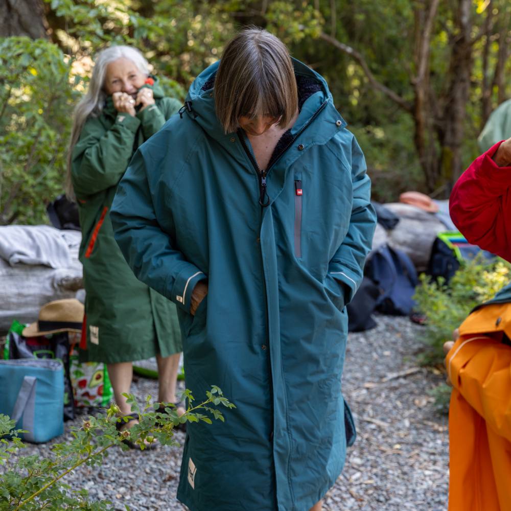 Female swimmer wearing a Red Alter Evo long sleeve waterproof changing robe in Deep Teal surrounded by other swimmers in a forest setting.
