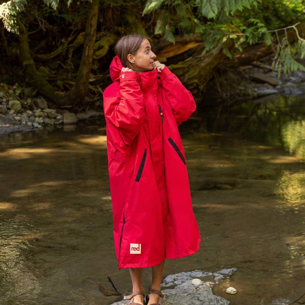 Woman stood on a stone by a river's edge, wearing a Red Alter Evo long sleeve waterproof changing robe in Siren Red.