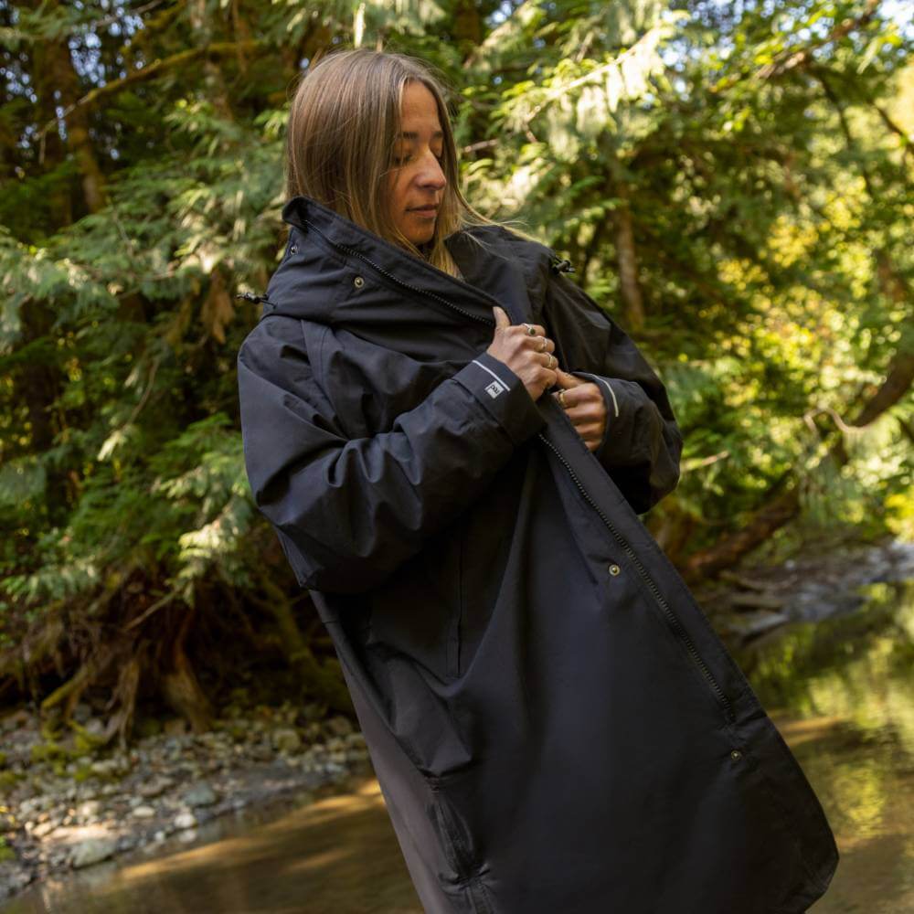 Woman standing by a stream in a forest, wearing a Red Alter Evo long sleeve waterproof changing robe in Stealth Black.