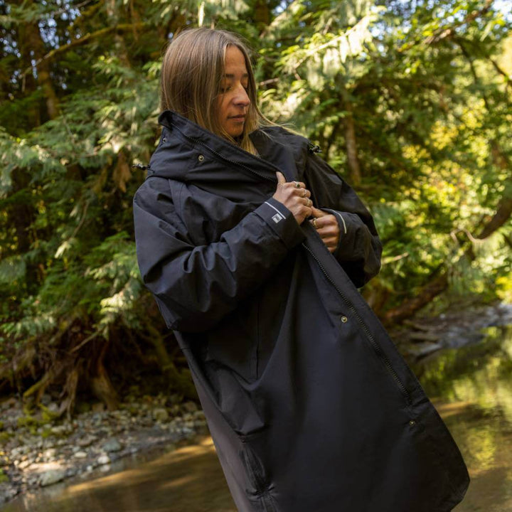Woman standing by a stream in a forest, wearing a Red Alter Evo long sleeve waterproof changing robe in Stealth Black.