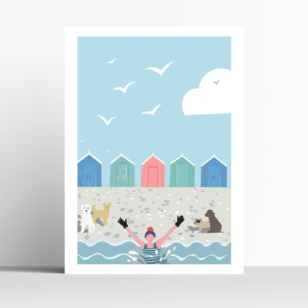An A4 art print with a white border, featuring a light blue sky, white seagulls, a white cloud, colorful beach huts, and a swimmer in the water with dogs on a pebble beach. 