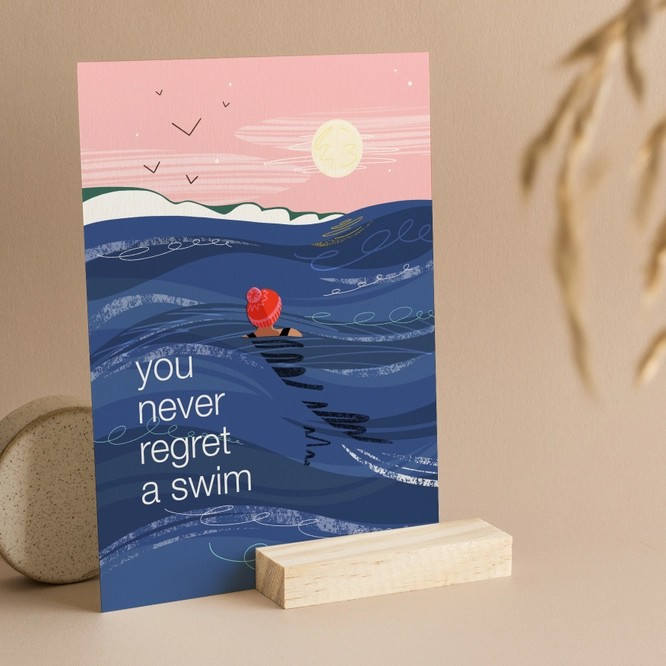 Greeting card with illustration of swimmer in bobble hat under the full moon, with text “You Never Regret a Swim.”