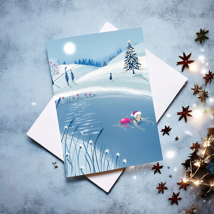 Flat lay of Tis The Season No1 Christmas card by Andrea Hall featuring a festive winter swimming scene under a glowing moon.
